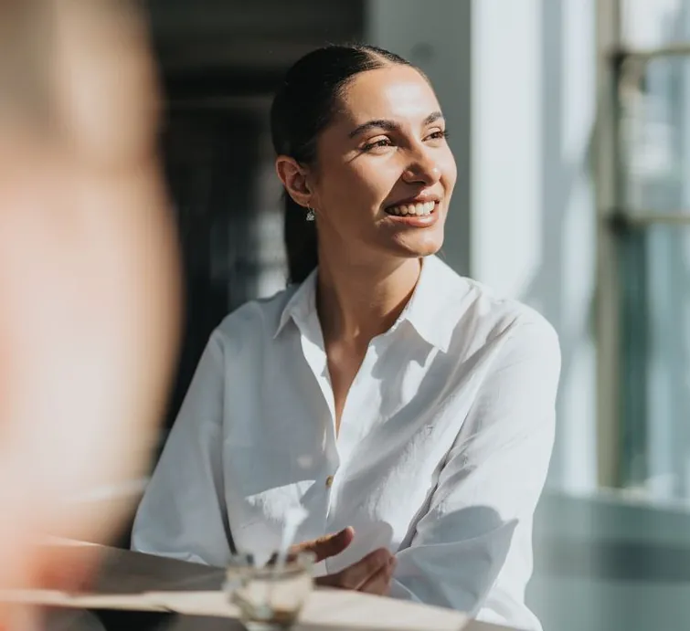 A smiling woman in a white shirt talking with a colleague