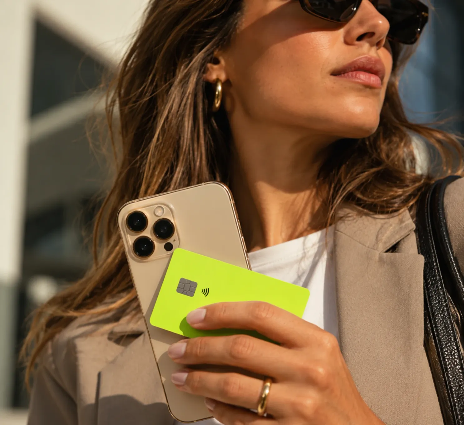 A woman in sunglasses holding a lime-green payment card against the back of her phone