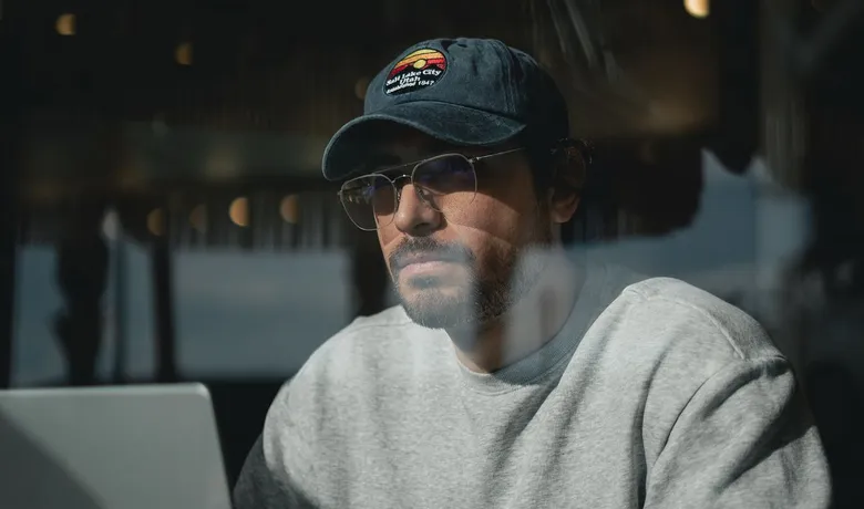 A man in a cap and sunglasses working on his laptop