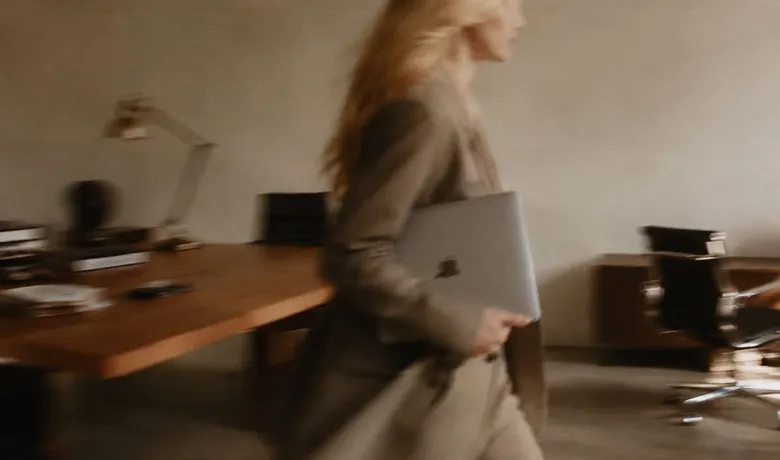A woman carrying a laptop through a softly lit office